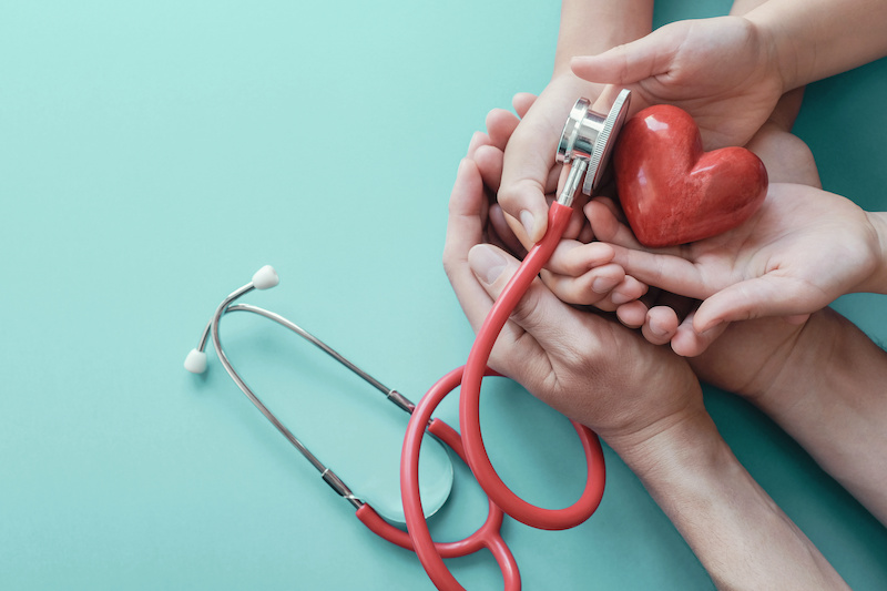 Family hands holding red heart with stethoscope, heart health, health insurance